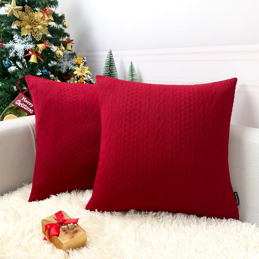Two red knit Christmas pillow covers with cable knit texture on a couch with a Christmas tree and gift.