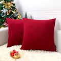 Two red knit Christmas pillow covers with cable knit texture on a couch with a Christmas tree and gift.