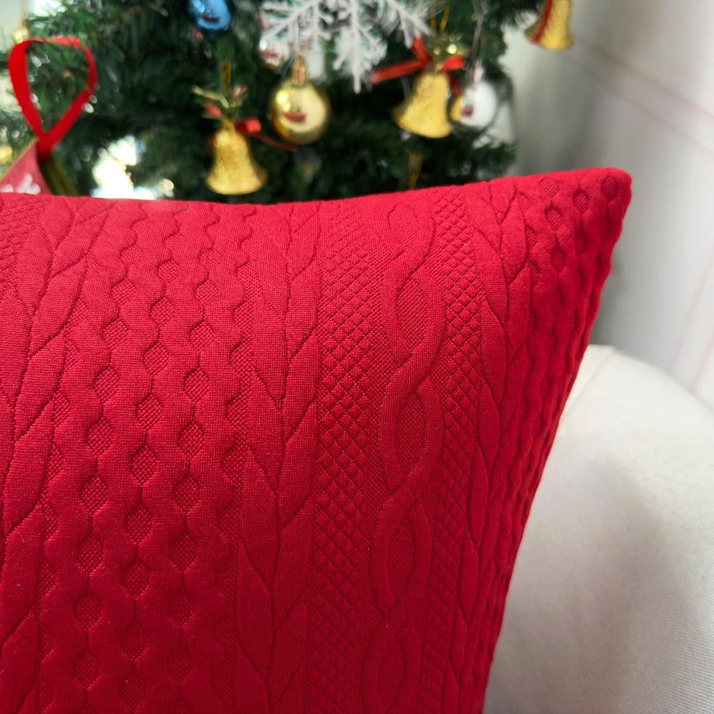 Red Christmas pillow cover with embossed knit texture, shown in front of a decorated Christmas tree.
