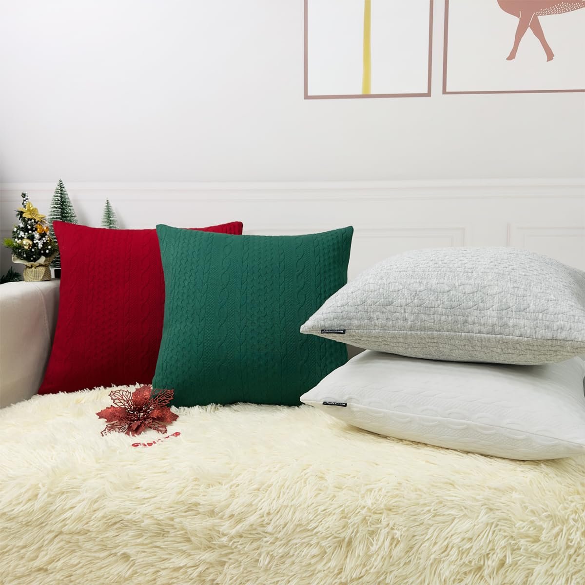 Four knit Christmas pillow covers in red, green, light grey, and white arranged on a fluffy white rug.