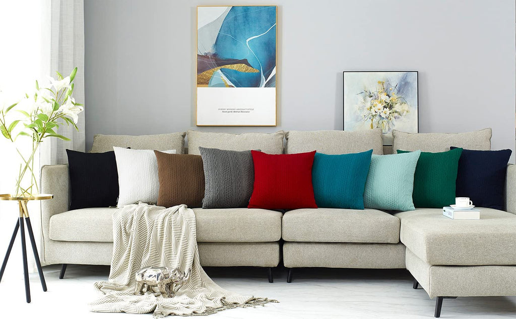 Assortment of knit throw pillow covers in various colors displayed on a sectional sofa with a blanket and decorative items.