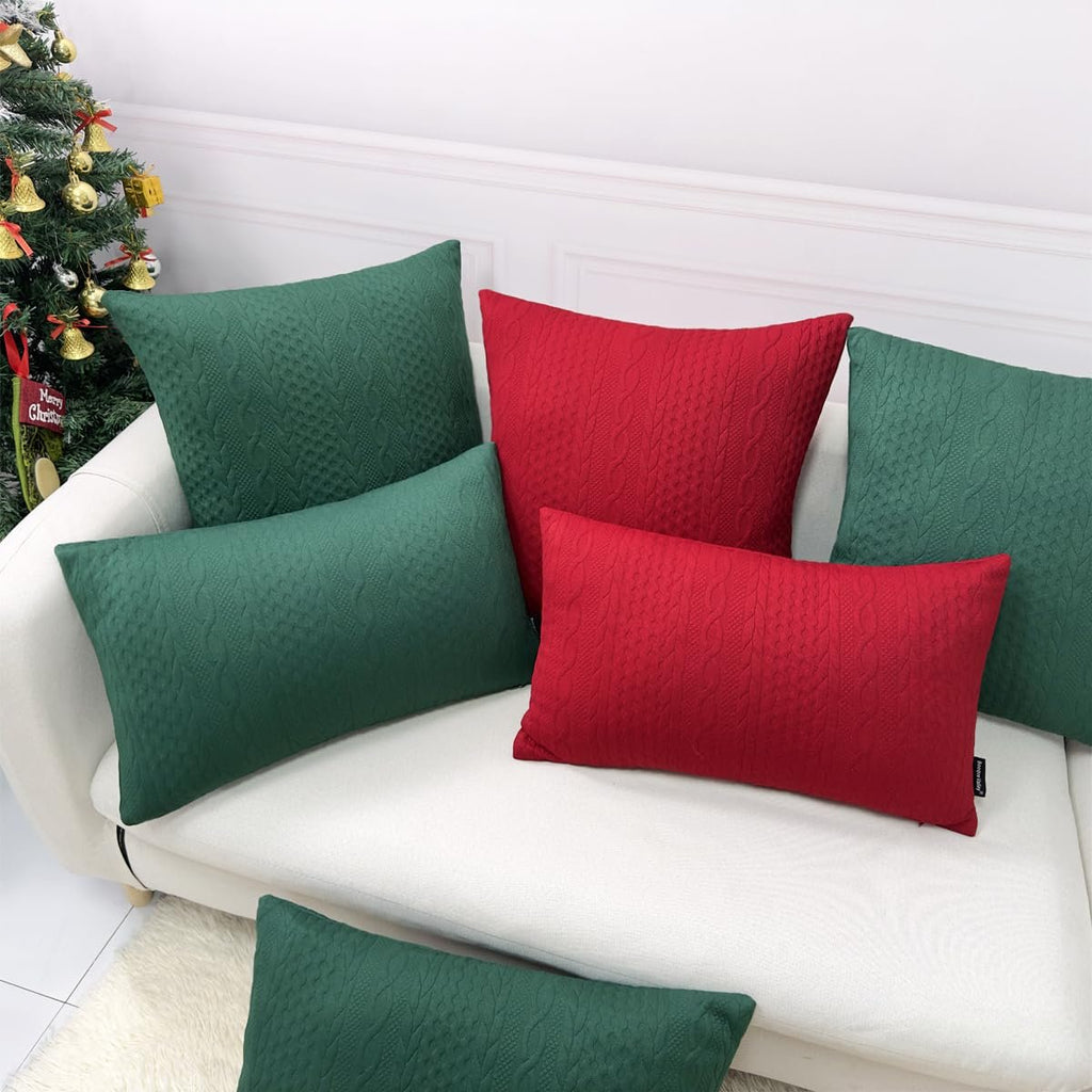 Christmas pillow covers in red and green with cable knit texture arranged on a white sofa next to a decorated Christmas tree.