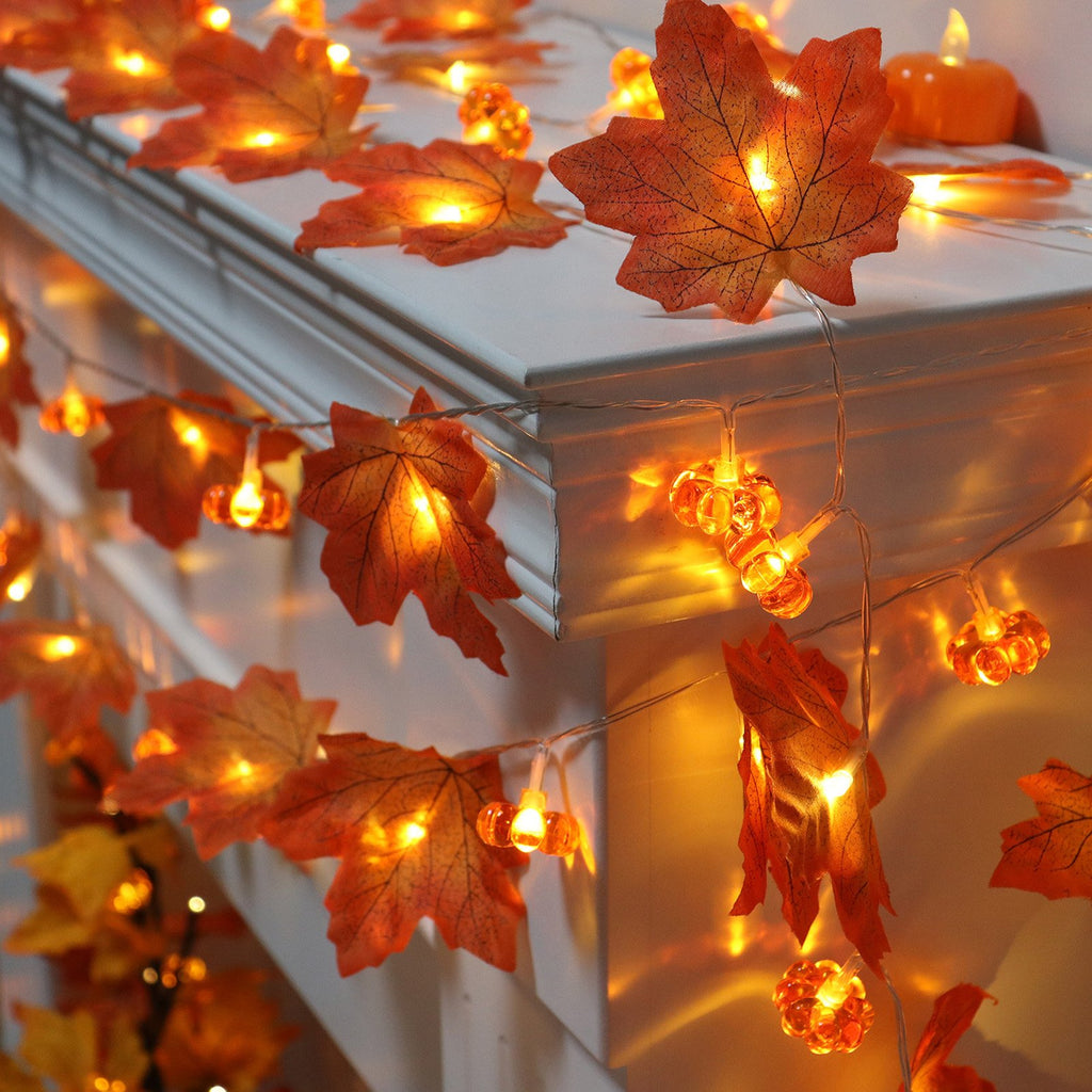 String lights with artificial maple leaves and pumpkin-shaped bulbs, illuminated with warm white LEDs, draped over a white ledge.