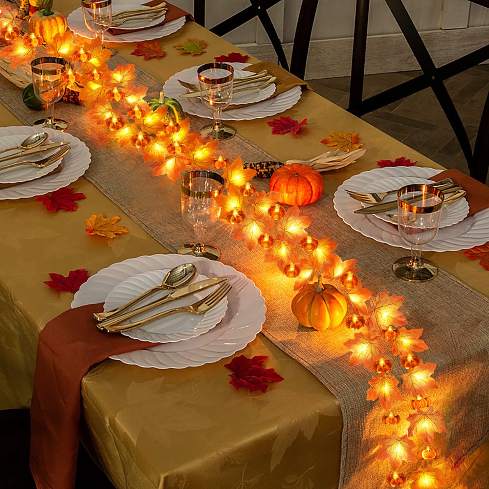 Thanksgiving table setting with a maple leaf and pumpkin string light garland draped across the center.
