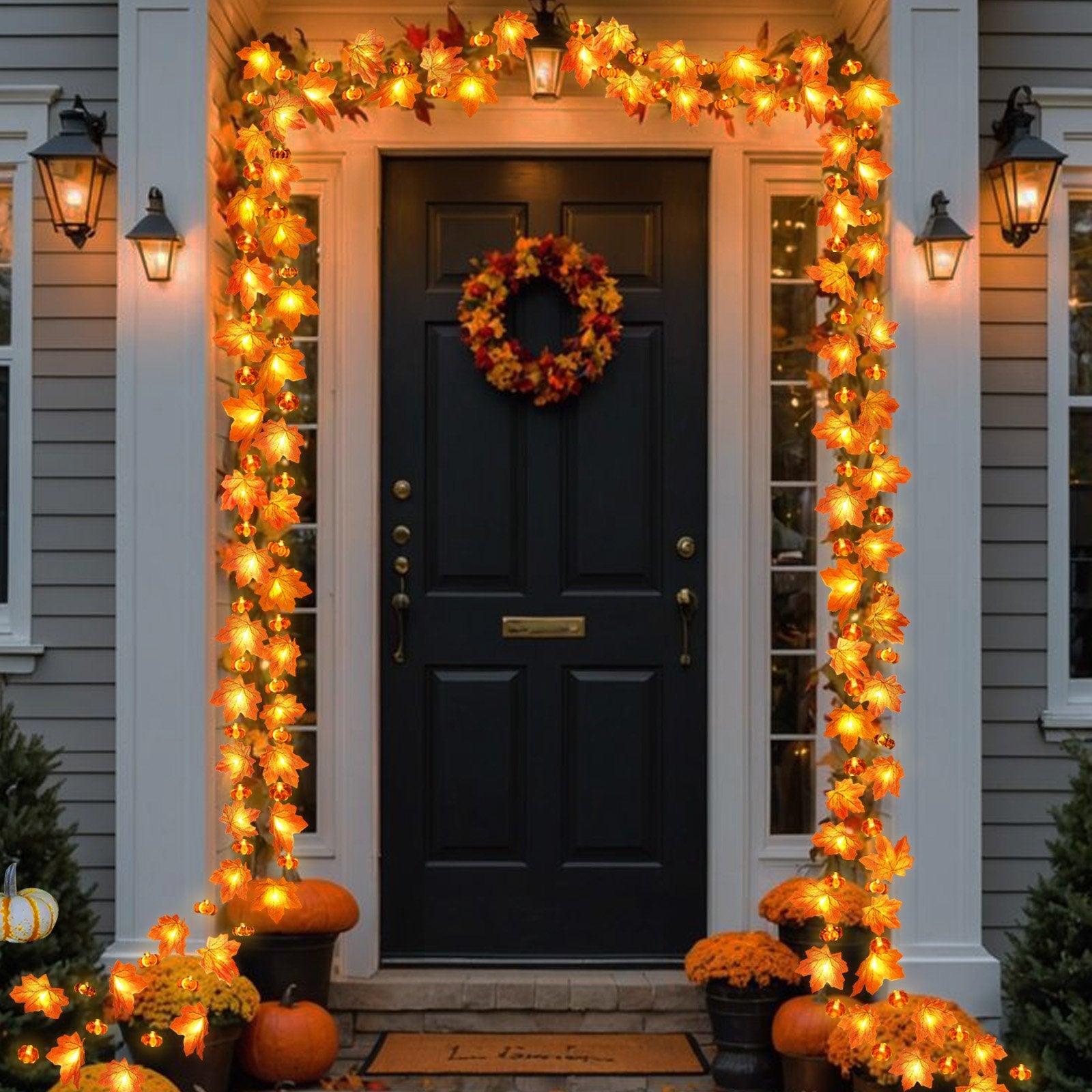 Front door decorated with a fall garland of maple leaves and pumpkins with warm white lights, flanked by lanterns and pumpkins on the porch.
