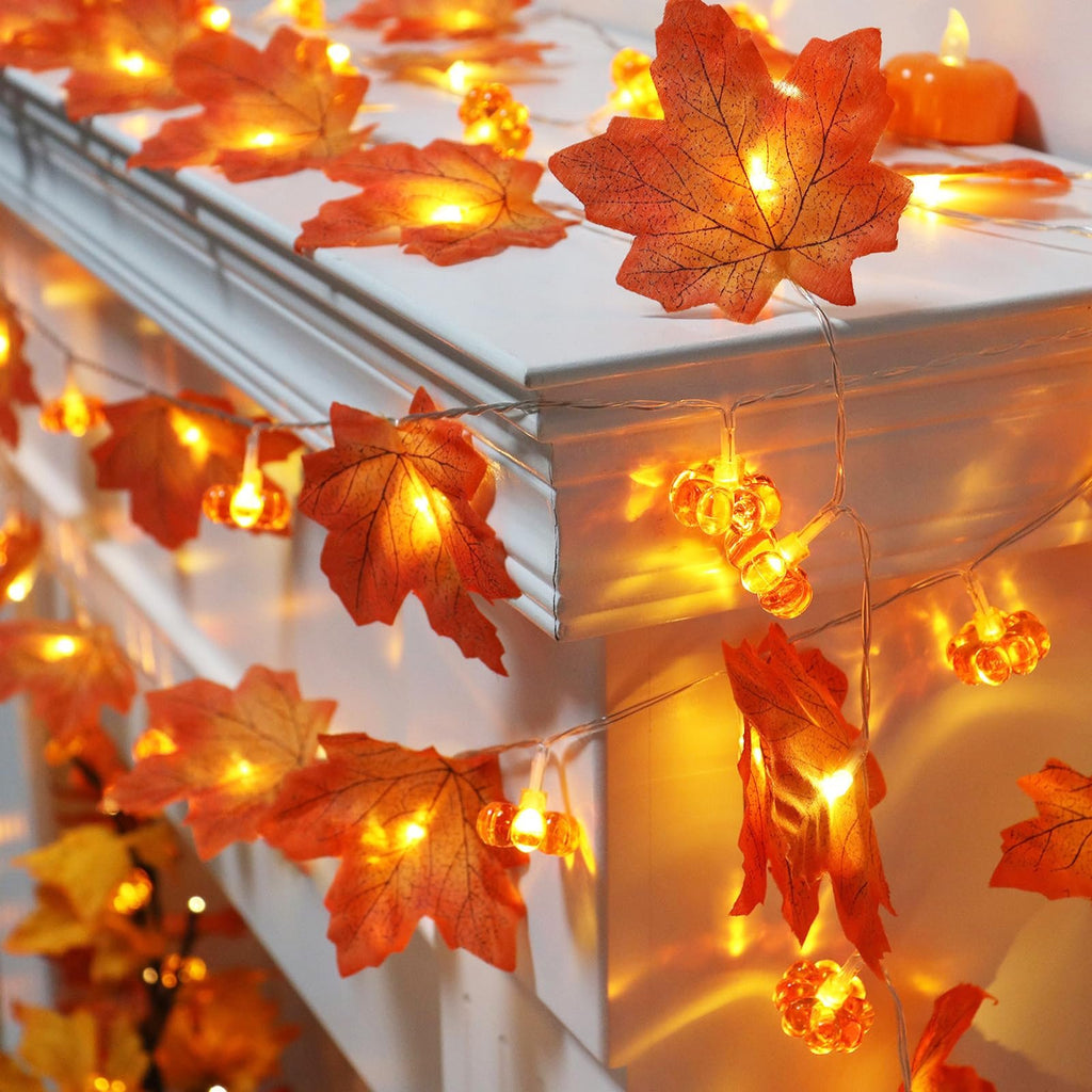 Fall garland string lights with maple leaves and pumpkin-shaped LEDs draped over a white surface.