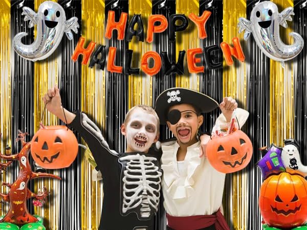 Two children in Halloween costumes pose in front of a black and gold fringe backdrop with 'Happy Halloween' balloons and ghost decorations.