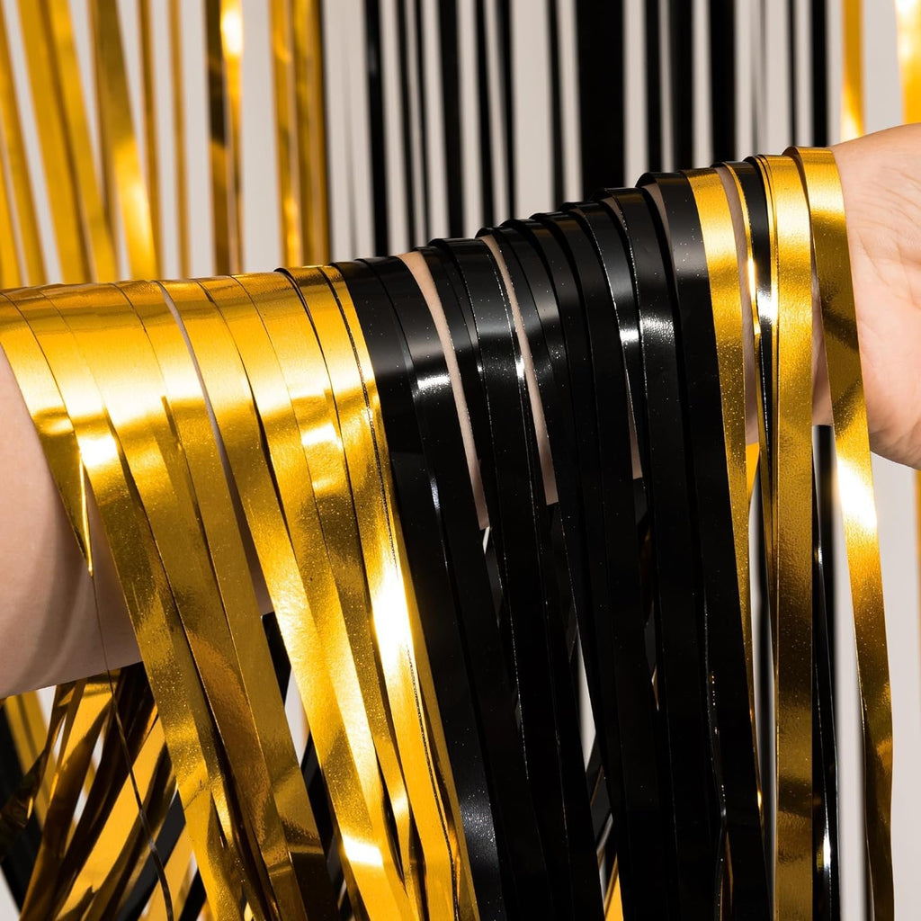 Close-up of a hand holding black and gold foil fringe curtains, showing the texture and shine of the streamers.