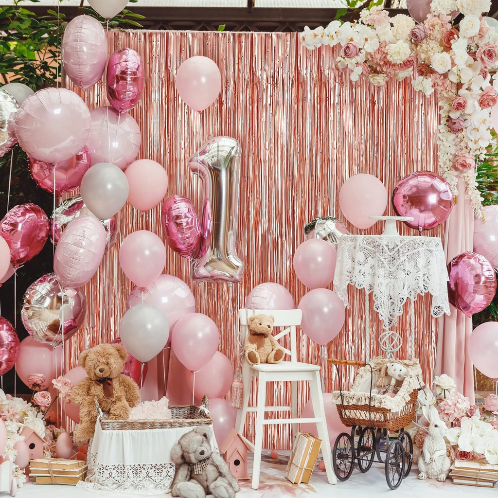 Rose gold foil fringe backdrop with pink and silver balloons, teddy bears, and a decorative carriage for a party setting.