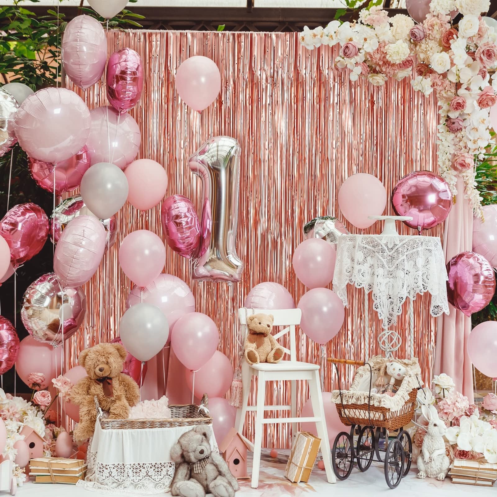 Rose gold foil fringe backdrop with pink and silver balloons, teddy bears, and a decorative carriage for a party setting.
