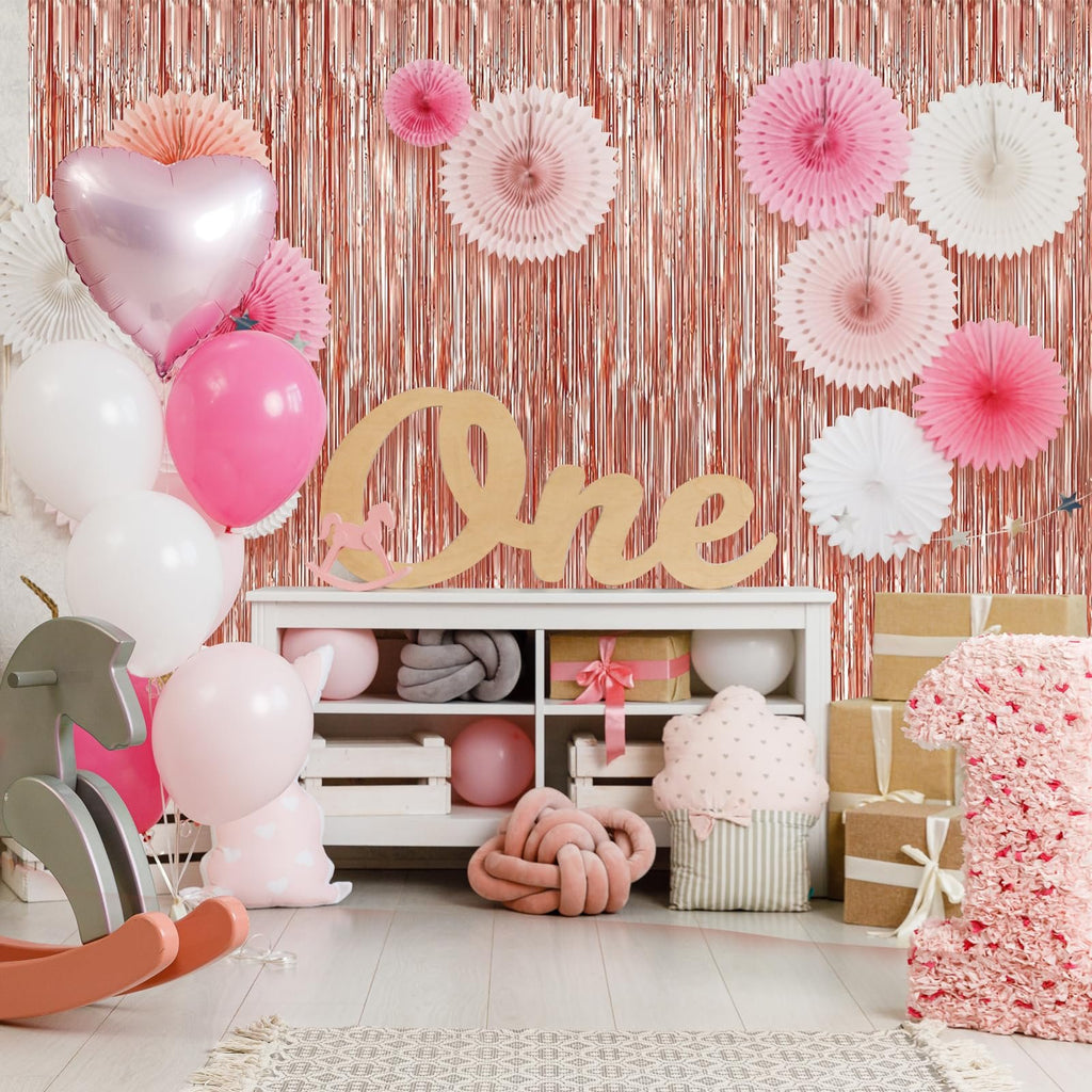 Rose gold foil fringe backdrop with pink and white decorations for a first birthday party.