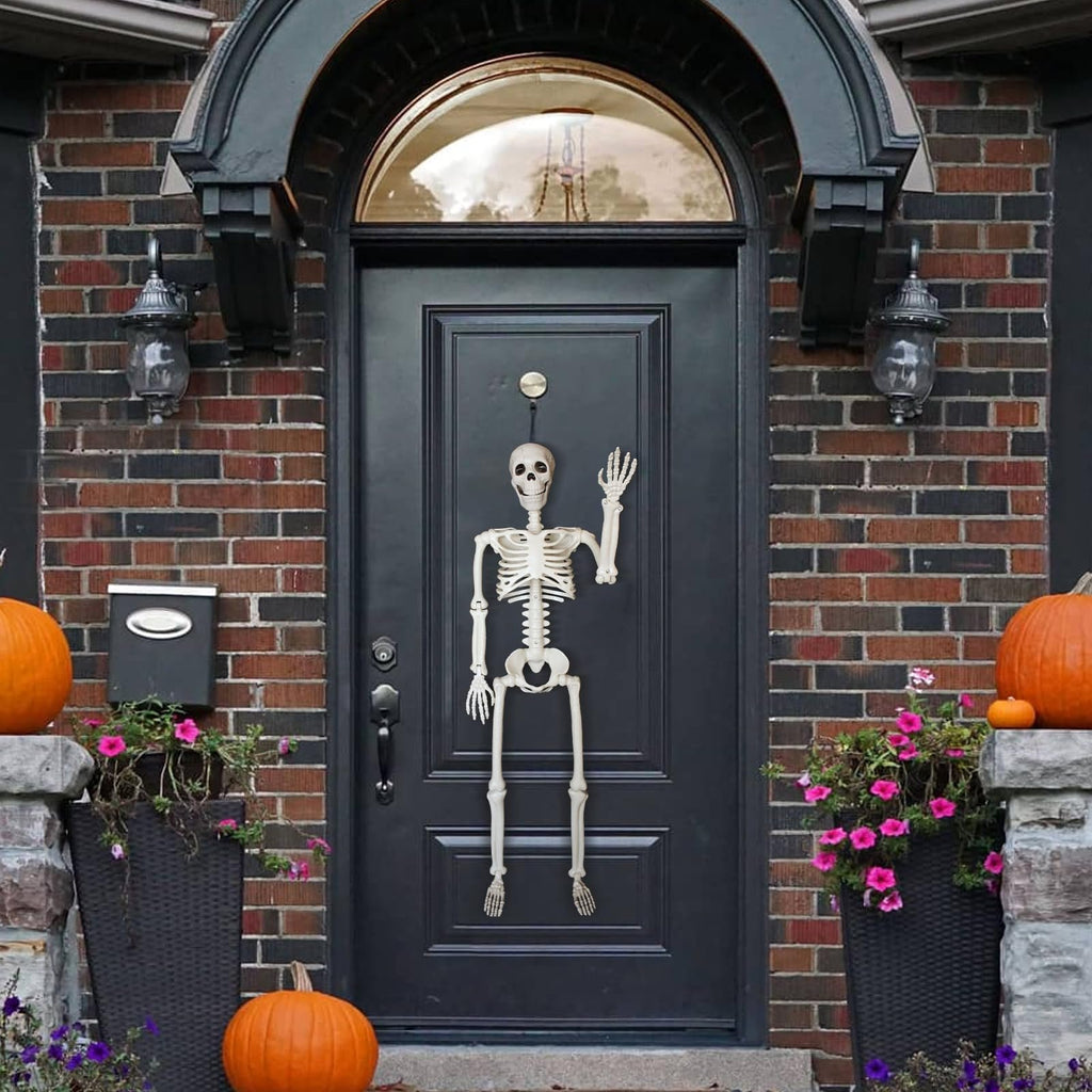 Posable skeleton decoration hanging on a black front door with pumpkins and flowers on the porch