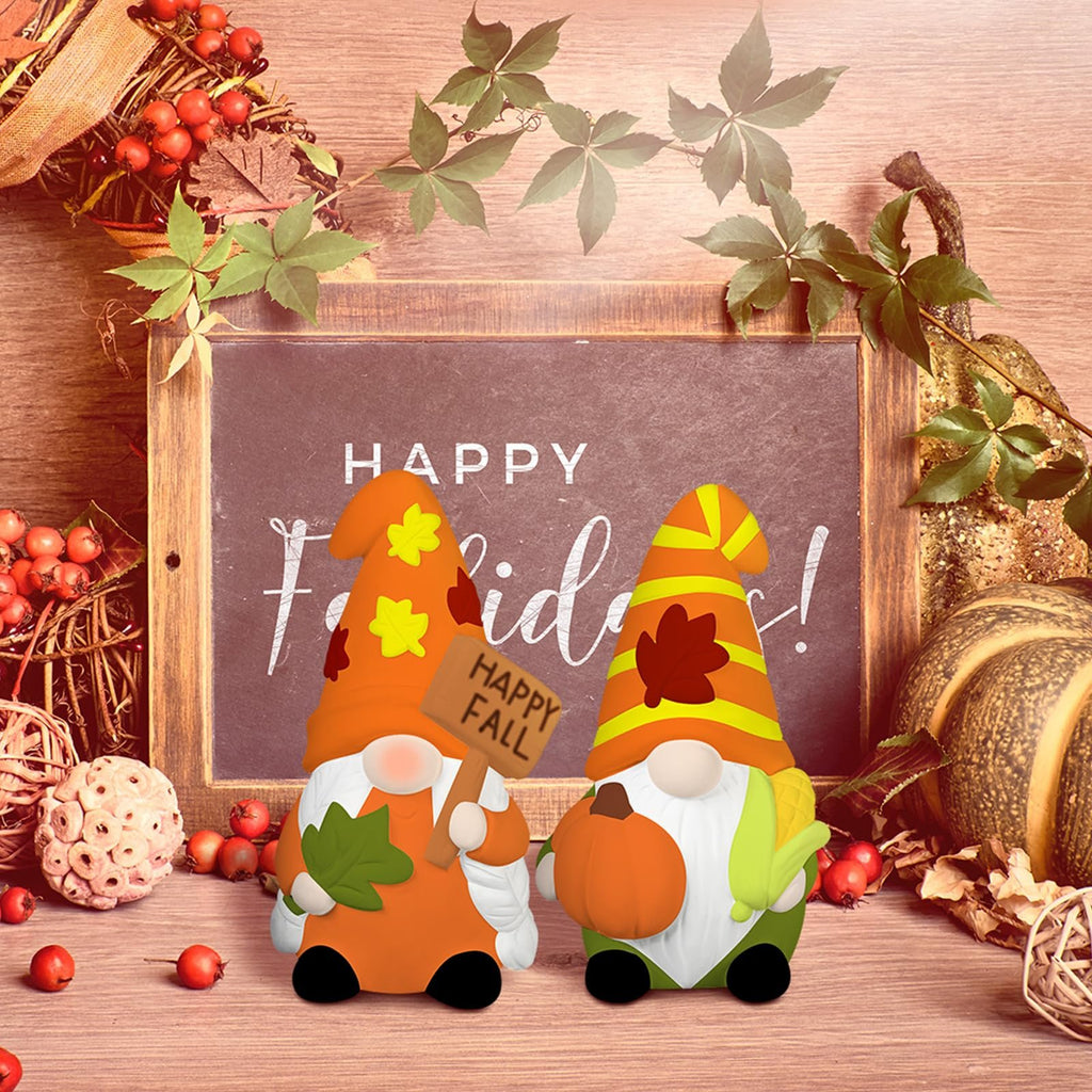 Two ceramic gnome statues with fall decorations, one holding a 'Happy Fall' sign.