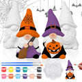 Two ceramic Halloween gnomes, one with a broom and orange hat, the other with a pumpkin and purple hat, surrounded by painting supplies.