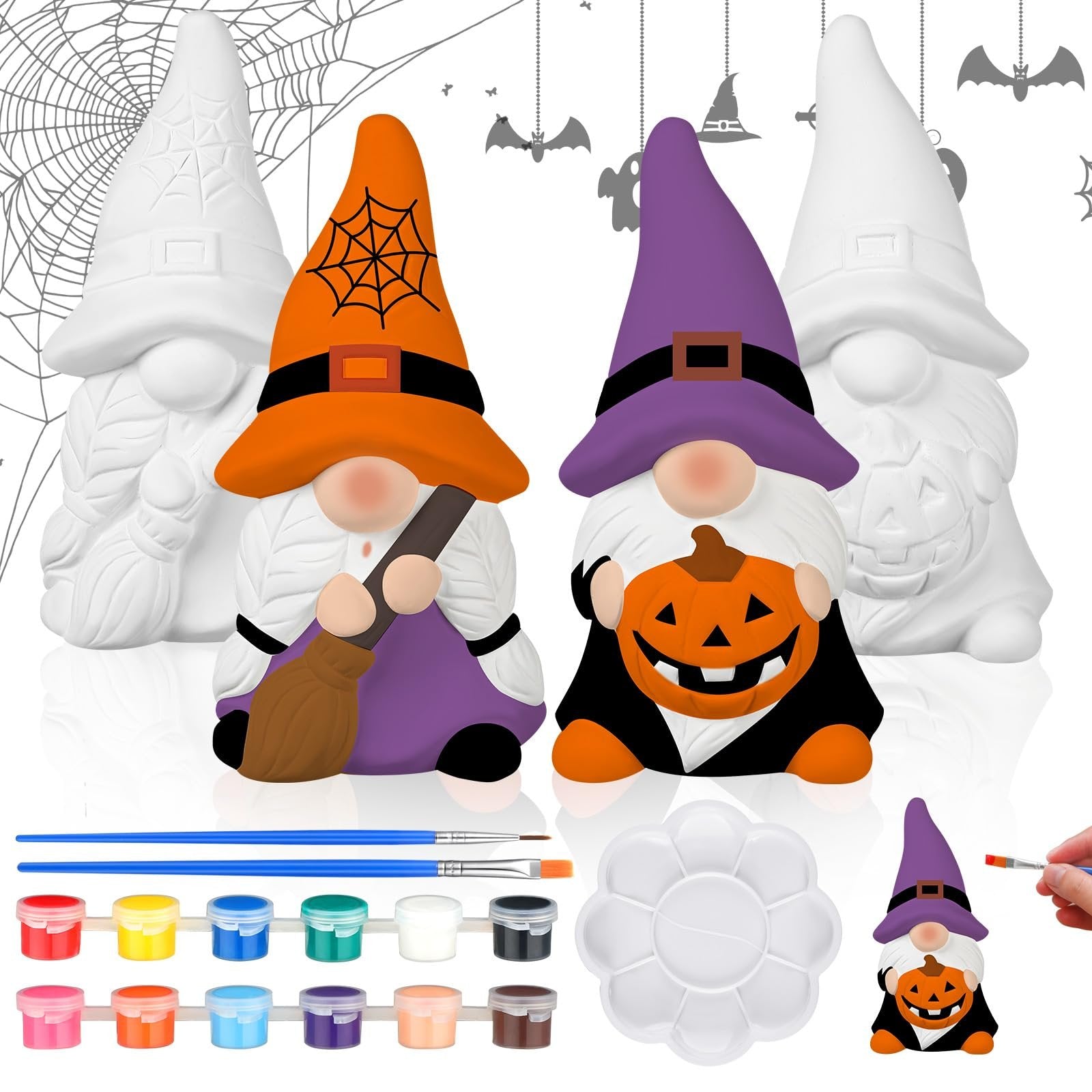 Two ceramic Halloween gnomes, one with a broom and orange hat, the other with a pumpkin and purple hat, surrounded by painting supplies.