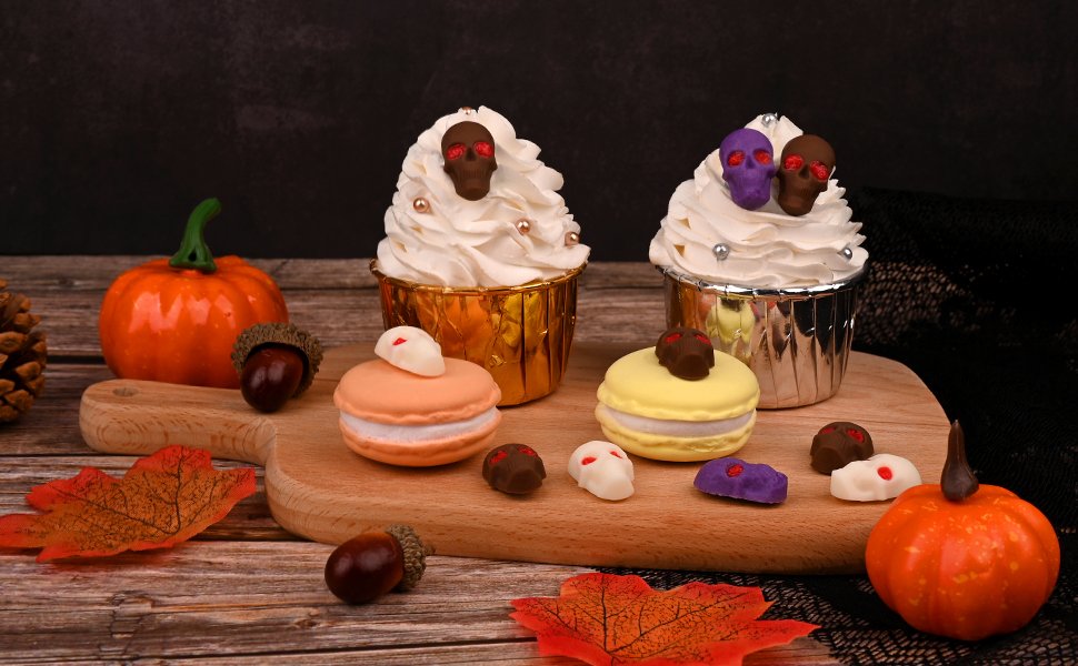 Halloween-themed cupcakes and macarons decorated with skull candies and acorns on a wooden board