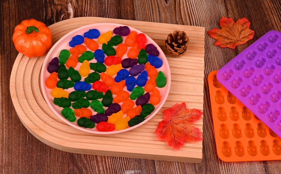 Skull-shaped silicone candy molds with colorful gummy candies and Halloween decorations