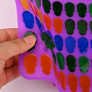 Hand holding a purple silicone candy mold with 40 skull-shaped cavities filled with colorful candy