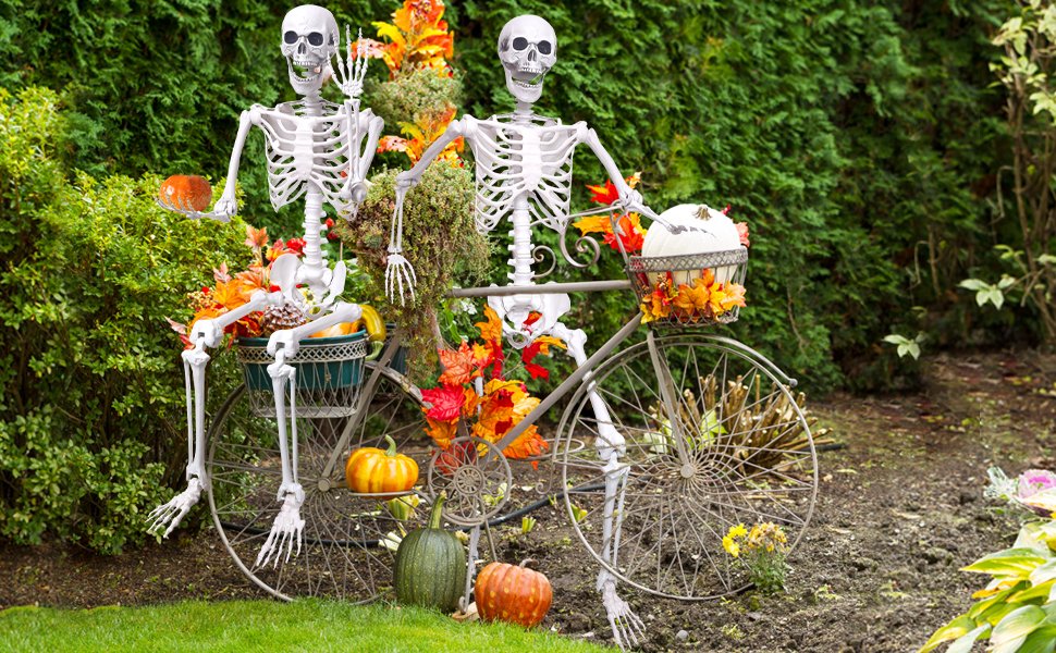 Two posable skeletons on a decorative bicycle with pumpkins and fall leaves for Halloween decor