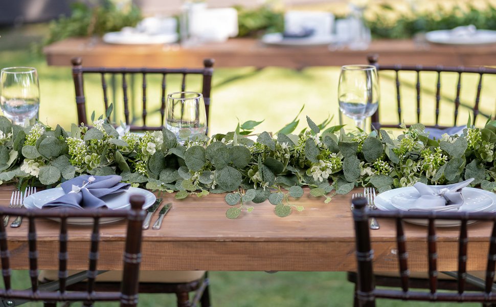 Faux eucalyptus garland with silk silver dollar leaves and plastic berries draped across a wooden table set for a meal.