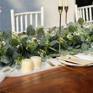 Faux eucalyptus garland with silver dollar leaves and white berries draped on a table with candles and place setting.