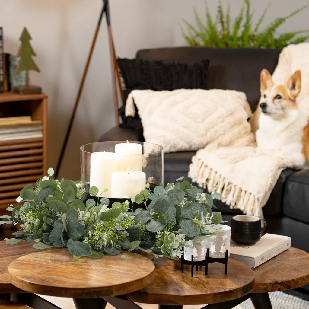 Faux eucalyptus garland with white berries arranged on a coffee table with candles and a dog on a couch in the background.