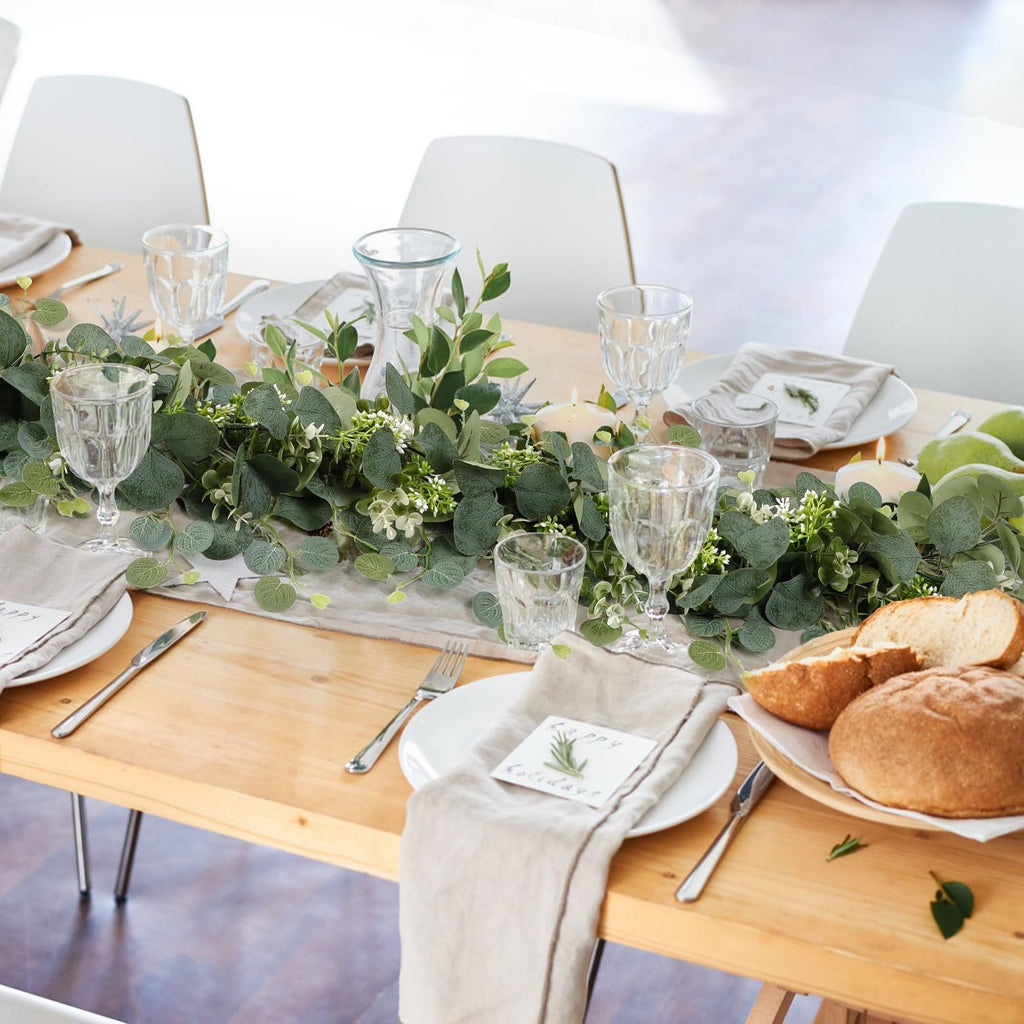 Faux eucalyptus garland with white flowers and berries draped across a table set for a meal.