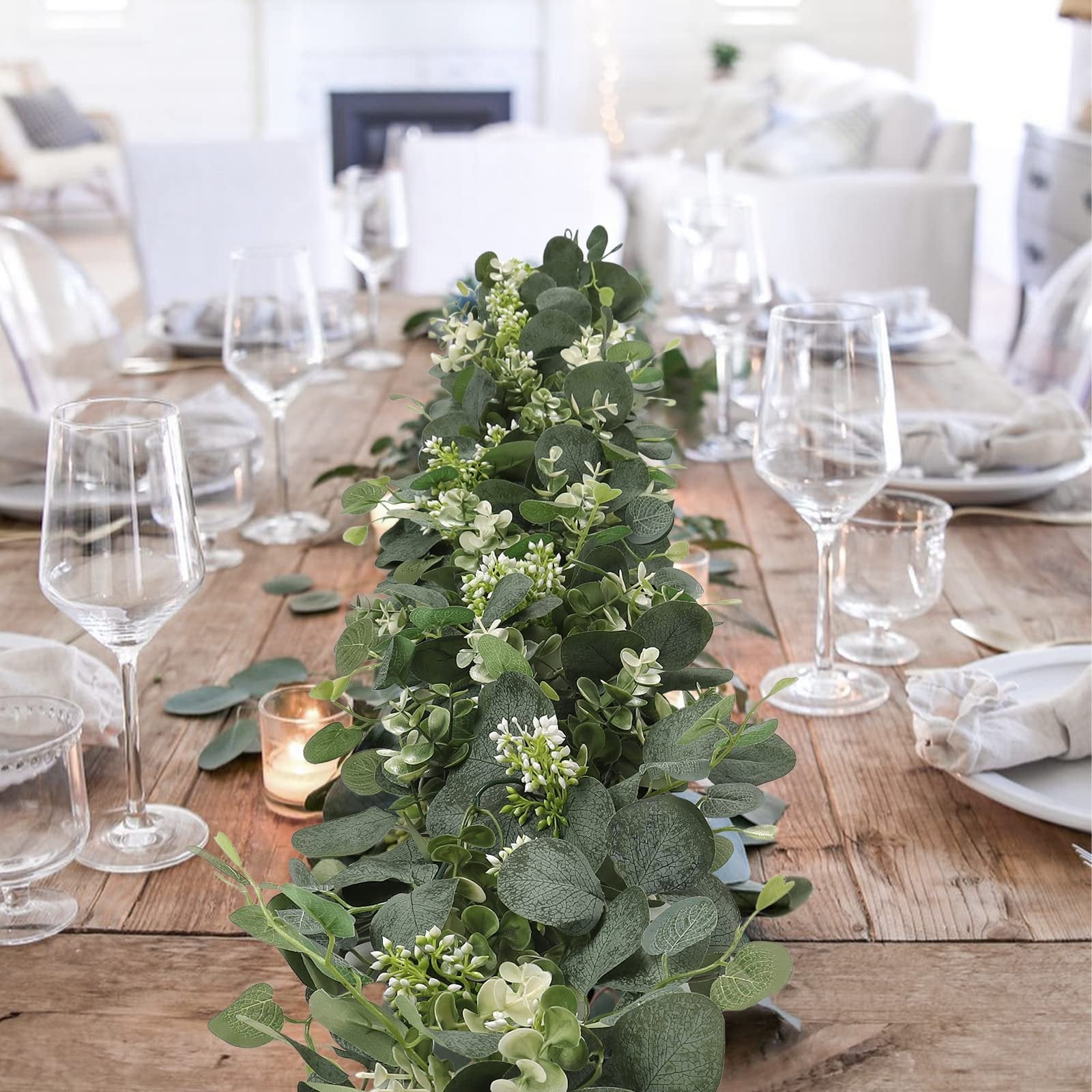 Faux eucalyptus garland with white flowers and berries draped on a wooden table with place settings and candles