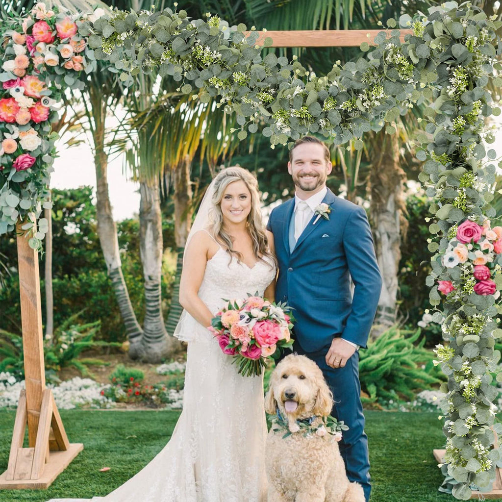 Wedding couple with dog under floral arch decorated with faux eucalyptus garland