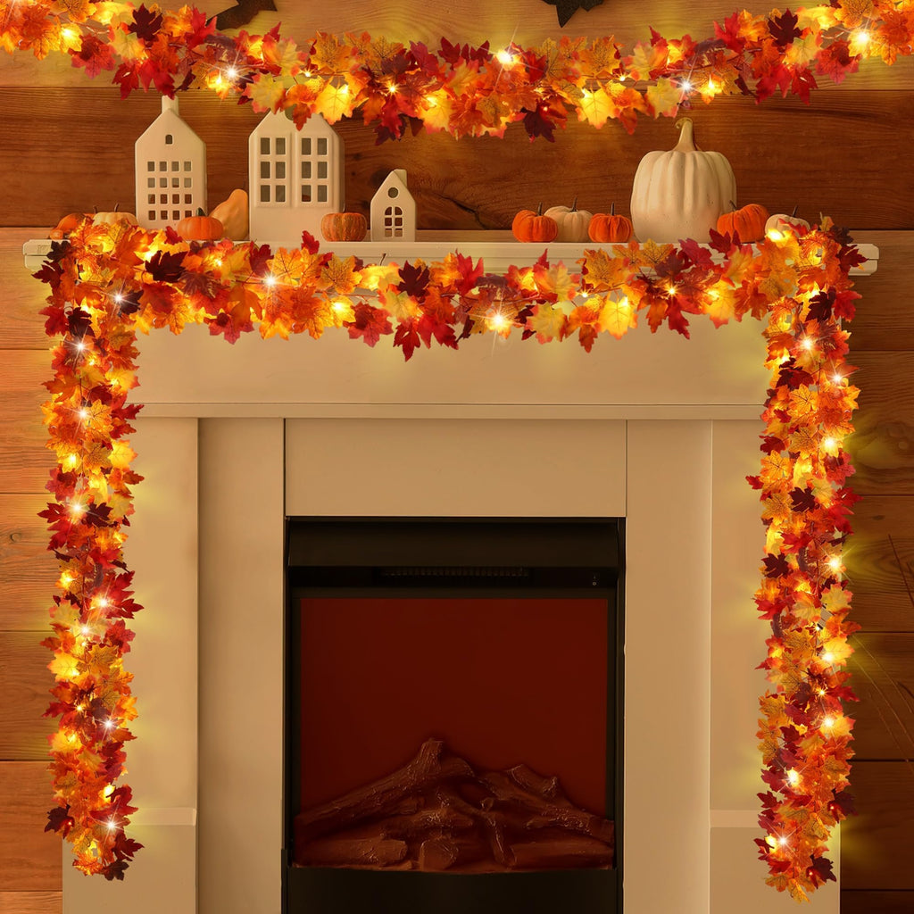 Artificial maple leaf garland with LED lights draped over a fireplace mantel with decorative houses and pumpkins.
