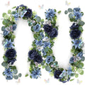 Artificial eucalyptus garland with navy blue flowers and silver butterflies arranged in a curve on a white background.