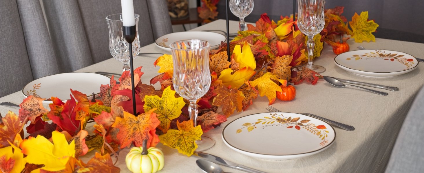 Autumn table setting with artificial maple leaf garland, plates, cutlery, and crystal glasses