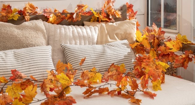 Artificial maple leaf garland draped over pillows on a couch, showcasing autumn colors.