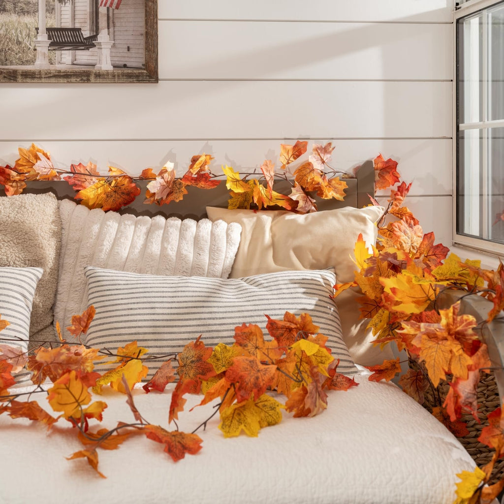 Artificial maple leaf garland draped over pillows and a bed with a framed picture in the background.