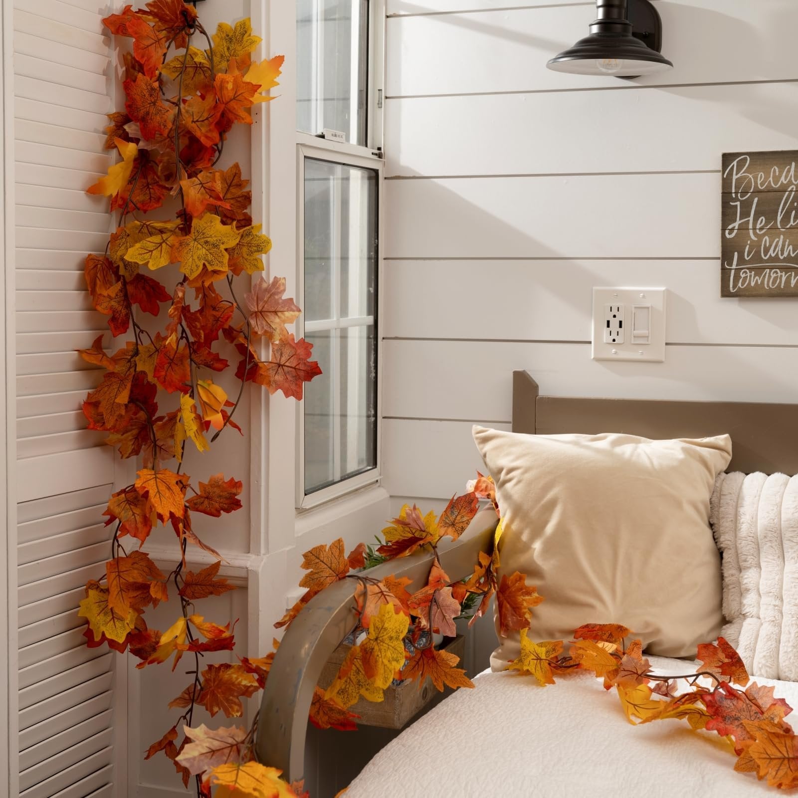 Artificial maple leaf garland draped along a window frame and bed, featuring autumn colors.