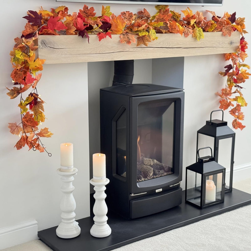 Artificial maple leaf garland with lights draped over a fireplace mantel with a wood beam.