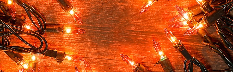 Close-up of orange mini string lights on a wooden surface, showing tangled green wires and illuminated bulbs.