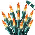 Cluster of orange mini string lights with green wire and plug on a white background