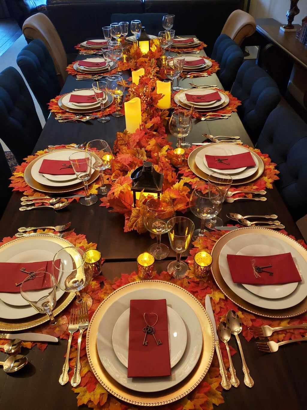 Thanksgiving table setting with fall leaves, candles, lanterns, and place settings for multiple guests.