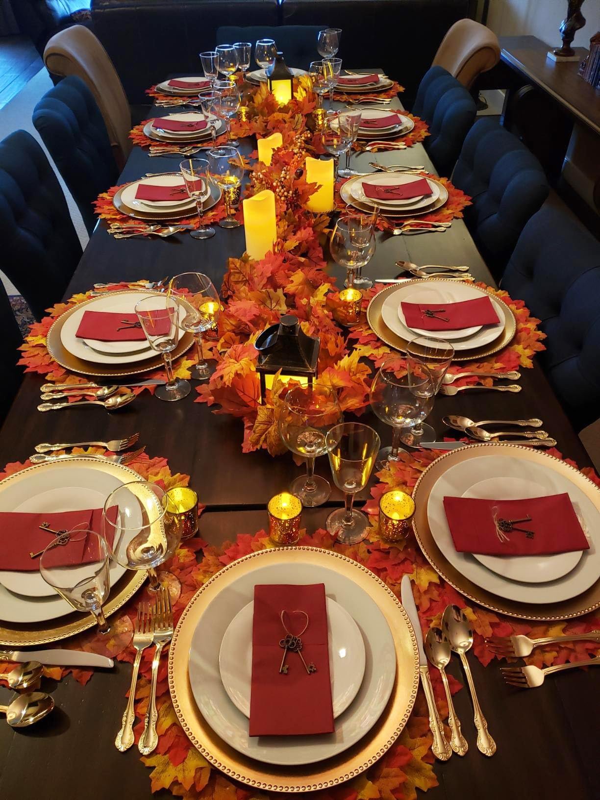 Thanksgiving table setting with fall leaves, candles, lanterns, and place settings for multiple guests.
