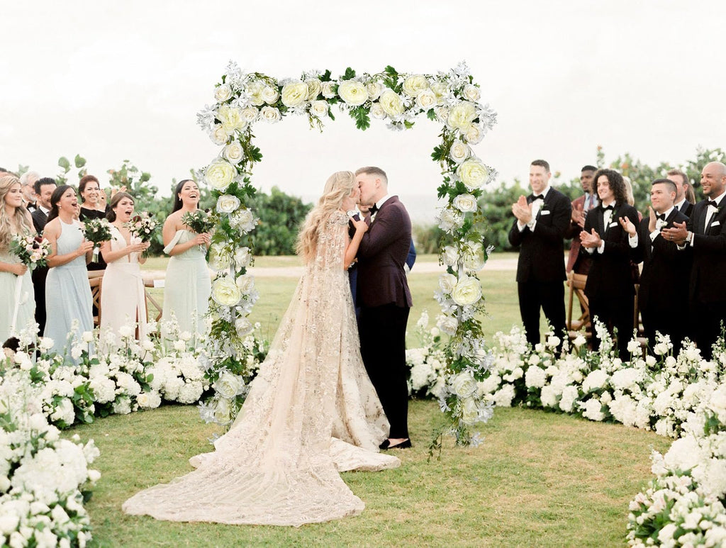 Wedding ceremony with floral arch and guests celebrating the couple's kiss