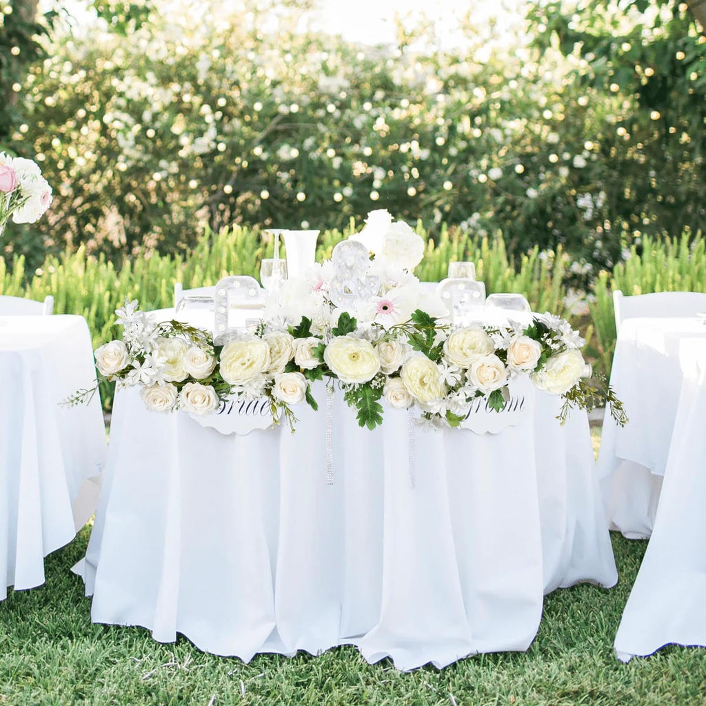Wedding sweetheart table decorated with white flowers and greenery, with 'Bride' and 'Groom' signs.