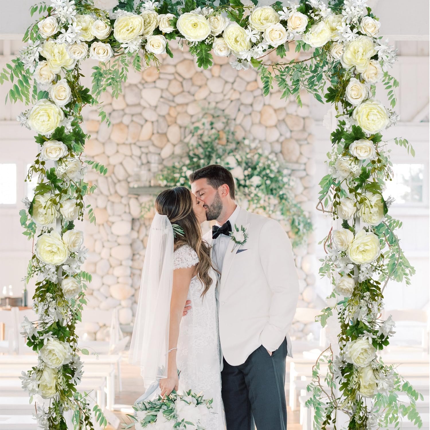 Wedding couple kissing under a floral archway decorated with white peonies and greenery