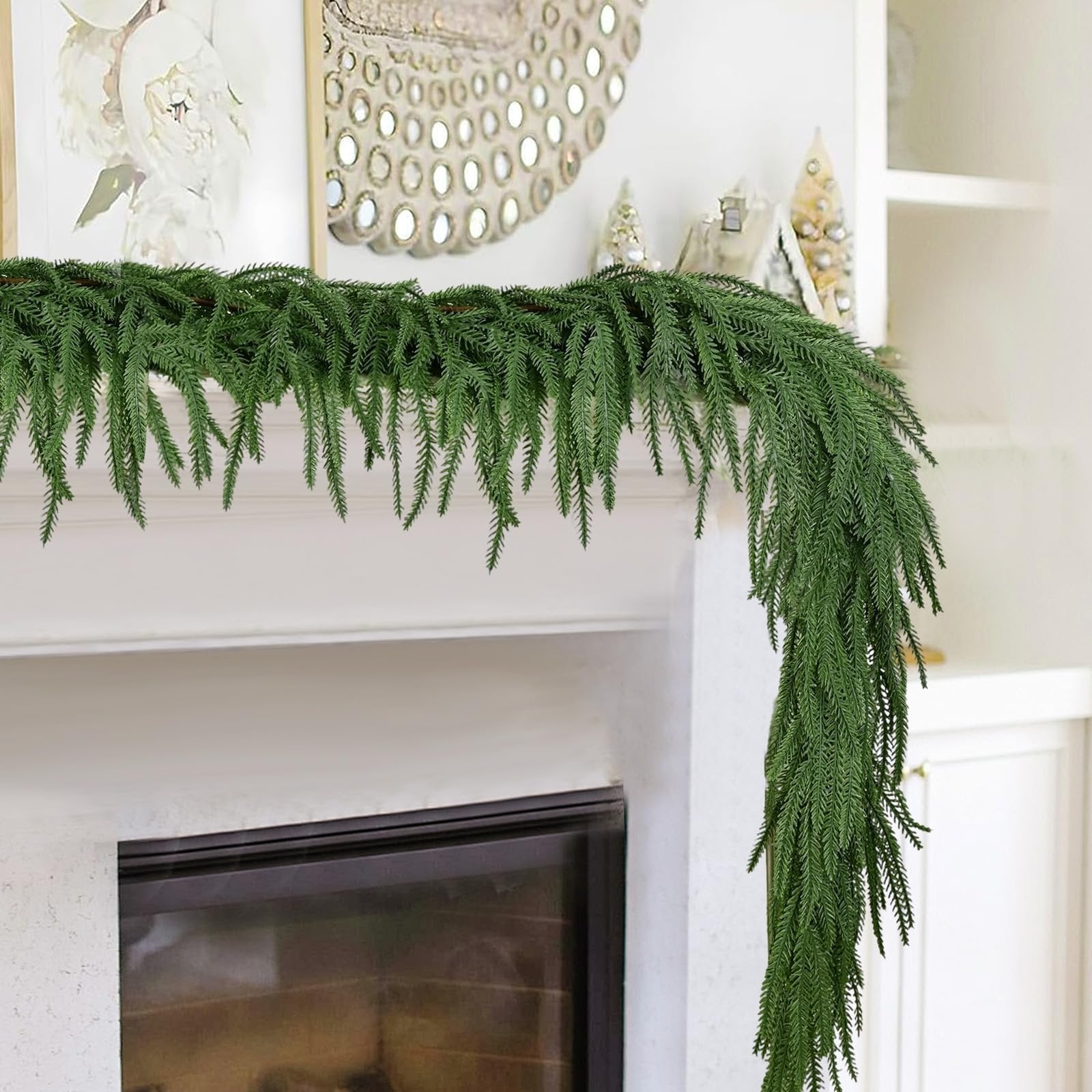 Artificial Norfolk pine garland with dense green branches draped over a white mantelpiece with a fireplace below.