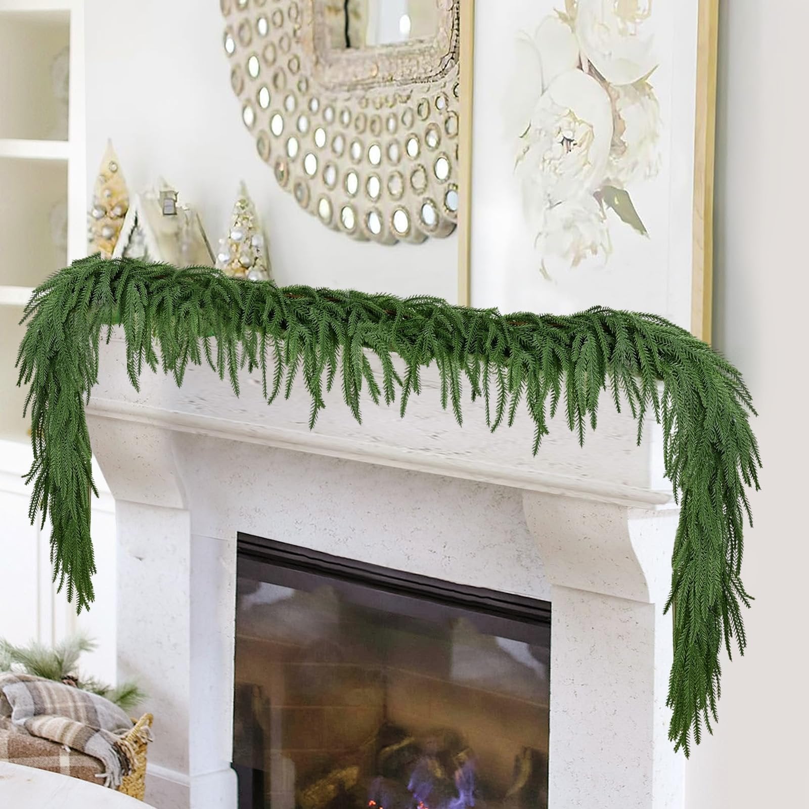 Artificial Norfolk pine garland draped over a fireplace mantel with decorative trees and a mirror in the background.