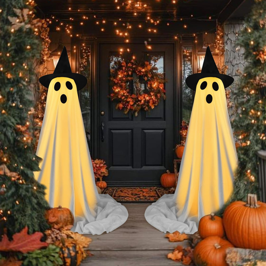 Two illuminated ghost decorations with witch hats stand on a porch with pumpkins and fall leaves for Halloween.