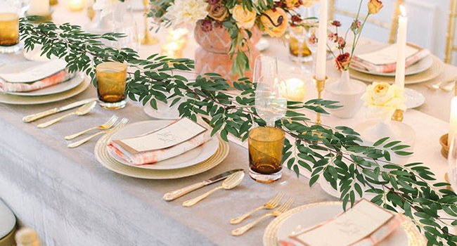 Artificial willow vine garland draped across a formal dining table setting with place settings and floral arrangements.
