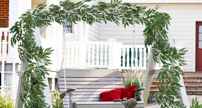 Artificial willow vine garland draped over a porch swing with red pillows