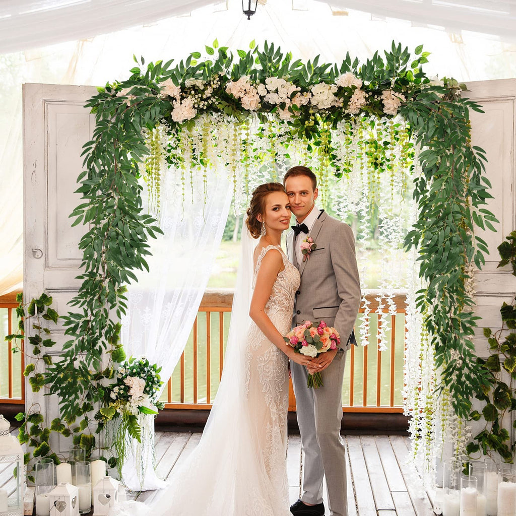 Bride and groom posing under a wedding arch decorated with artificial willow vines and white flowers