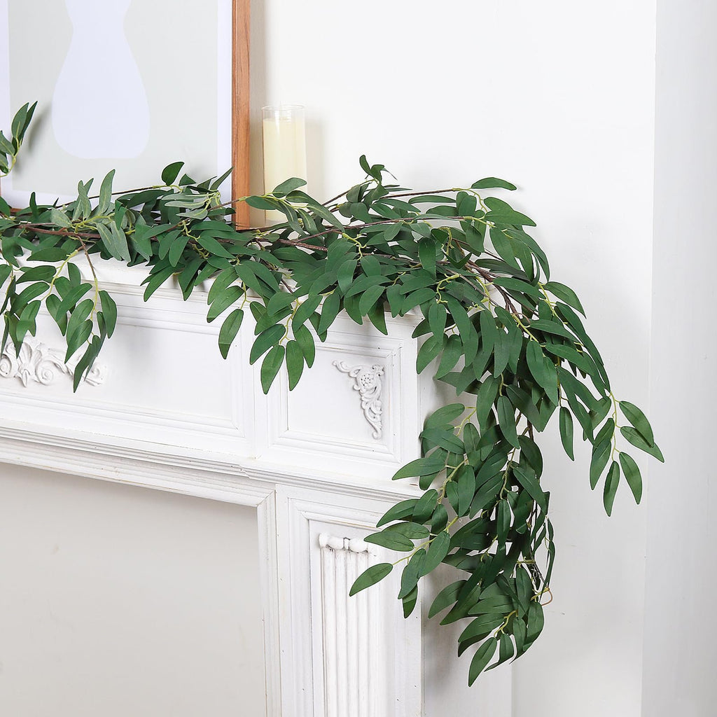 Artificial willow vine garland with green leaves draped over a white mantelpiece with a framed picture and candle
